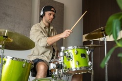 Young man professionally plays drums in specifically equipped music studio. Guy seems to really enjoy process. Man in headphones wears casual clothes