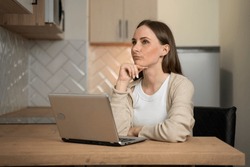 The woman is tired, she is bored to work remotely with a laptop, she burns out and is overloaded with work with employees with a clouded brain in the kitchen. 