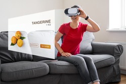 WOman sitting at home on the sofa with vr glasses buying grocery fruit food products.