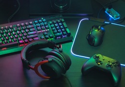 gamer work space concept, top view a gaming gear, mouse, keyboard, joystick, headset, mobile joystick, in ear headphone and mouse pad with rgb color on black table background.