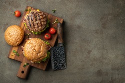 Tasty grilled home made burger with beef, tomato, cheese, bacon and lettuce on a dark stone background with copy space. Top view. fast food and junk food concept. Flat lay