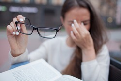 Closeup portrait of attractive female with eyeglasses in hand. Poor young girl has issues with vision. She rubs her nose and eyes out of fatigue. A student tired to study and read books.