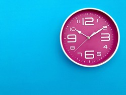 Closeup pink wall clock  set on blue background. The concept of 
