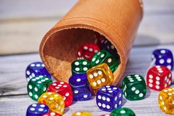 View to different colored game dices and a dice cup on a wooden table.