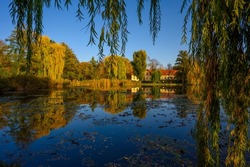 Village pond with reflections of colorful trees in the water and an old manor in the sunset.