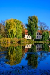 Village pond with reflections of colorful trees in the water and an old manor in the background.