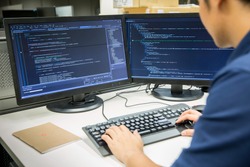 Male programmer working on desktop computer at white desk in office.