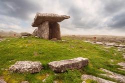 Poulnabrone Dolmen relict building in County Clare near Ballyvaughan town, Ireland, Beautiful cloudy sky and background in a haze. Green grass in foreground. Irish national monument