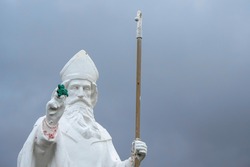 White statue of Saint Patrick holding green shamrock at the start of foot path to the peak of Croagh Patrick, county Mayo, Ireland.