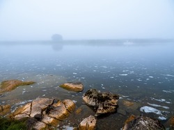 Warm orange color rocks in a river or lake and cool fog in the background. Calm water surface. Beautiful nature scene. Nobody, selective focus. Warm and cool tone.
