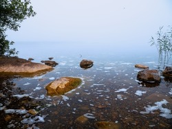 Warm orange color rocks in a river or lake and cool fog in the background. Calm water surface. Beautiful nature scene. Nobody, selective focus. Warm and cool tone. Misty weather