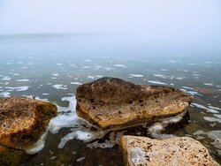 Warm orange color rocks in a river or lake and cool fog in the background. Calm water surface. Beautiful nature scene. Nobody, selective focus. Warm and cool tone. Misty weather