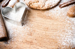 Christmas and holiday baking background, flour, bakeware, heart, cinnamon, cookies and almonds on a wooden board, viewed from above