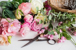 Fresh flowers, leaves, and tools to create a bouquet on a table, florist's workplace.