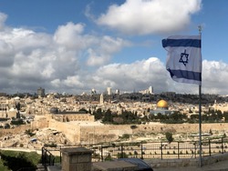 Israeli flag with a Star of David flying over Jerusalem; with Dome of the Rock and the Temple Mount, the rooftops of the Old City and the new city of West Jerusalem skyline in the background