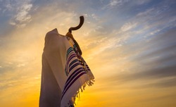 Blowing the shofar for the Feast of Trumpets - Jewish man in a traditional tallit prayer shawl blowing the ram's horn against dramatic sunset sky