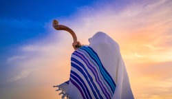 Blowing the shofar for the Feast of Trumpets - Jewish man in a traditional tallit prayer shawl blowing the ram's horn against beautiful sunset sky