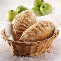 Round brown bread  with seeds and spices and some green apples as background