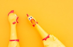 Surprised chicken toys are isolated on a orange background, one looks at the camera and shouts, the other one to the side. Screaming chicken toys on a yellow background.