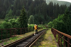Couple in love hugging and kissing on a railway bridge in the mountains standing on the track. Tourists in love kissing against the backdrop of a beautiful landscape of cradles and forest in mountains