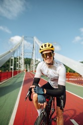 Male professional cyclist in outfit stands on the street with a bicycle and poses for the camera with a smile on his face on a sunny summer day