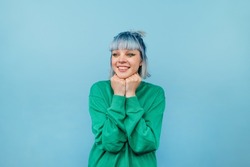 Happy hipster girl with colored hair stands on a blue background with a smile on his face and joyful looks away.