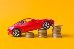 Red toy car rides up a stack of coins