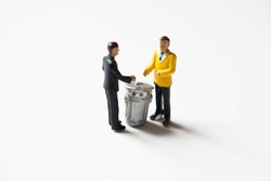 Miniature business men shaking hands over a garbage can. Scam or dishonest scheme. Corruption or ripoff. A bad deal where investments are lost.