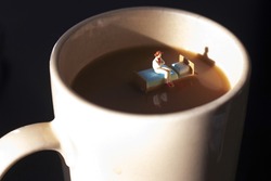 Miniature woman on a bed in a cup of coffee. Waking up with caffeine to start day. Time to start your morning with a hot cup of java. Coffee is a big part of our day.  Insomnia or exhaustion concept. 
