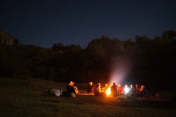 amazingly beautiful landscape with a view of the starry sky in the mountains of Crimea and a group of tourists singing songs by the fire with a guitar