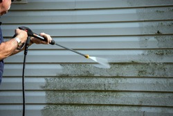 An unidentified man uses a power washer to clean mold and grime off the siding of a house.