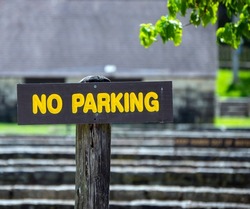 A wooden sign with bright yellow letters makes it clear to drivers that parking is not allowed in this location. Bokeh effect