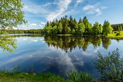 Scenic view of a Kladska lake in the Czech Republic, close to Marianske Lazne surrounded with forest. Sunny summer landscape with blue sky and white clouds and reflection in water.