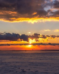 Silhouettes of people walking on a snow covered beach under a vibrant orange sunset sky. Jones Beach State Park - Wantagh New York