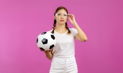 Young asian woman wearing white t-shirt and plant with goggle glass holding a ball in a concept of world cup soccer football champianship game on the pink screen background.