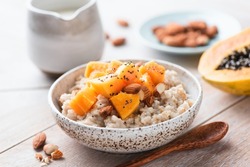 Oatmeal porridge bowl with papaya, chia seeds and almond nuts on a wooden table background, closeup view