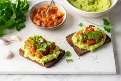 Rye bread toast with mashed avocado and roasted beans in tomato sauce. Tex mex, mexican style healthy vegan avocado appetizer