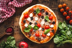 Pizza with tomatoes, mozzarella cheese, black olives and basil. Delicious italian pizza on wooden pizza board. Table top view