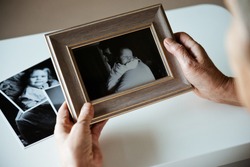 An elderly woman is holding a frame with a black and white  photo. Sentimentality on father's day.