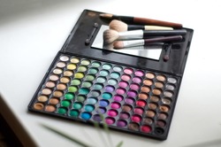 A palette with multi-colored eye shadow and makeup brushes on the windowsill