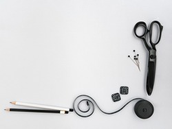 Assorted monochrome craft and sewing tools. Scissors, buttons, pins and measuring tape lying on grey background with copy space. Bottom frame, mock up for tailoring or dressmaking business design.
