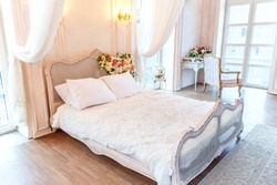 Beautiful luxury classic white bright clean interior bedroom in baroque style with king-size bed, large window, armchair and flower composition