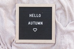 Autumnal Background. Black letter board with text phrase Hello Autumn lying on white knitted sweater. Top view flat lay. Thanksgiving banner. Hygge mood cold weather concept