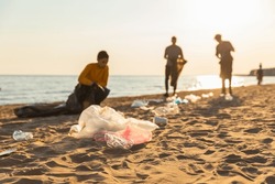 Earth day. Volunteers activists collects garbage cleaning of beach coastal zone. Woman and mans puts plastic trash in garbage bag on ocean shore. Environmental conservation coastal zone cleaning