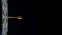 Golden dart arrow in the bullseye of a dart board against a black background