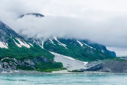 A view mist decending on the rocky, verdant shoreline close to the Margerie Glacier in Glacier Bay, Alaska in summertime