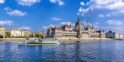 A ferry boat passes along the eastern shore of the River Danube in Budapest past the Parliament building in summertime