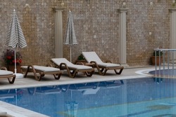 Three brown sunbeds with biege matresses and two striped umbrellas against mosaic wall with columns