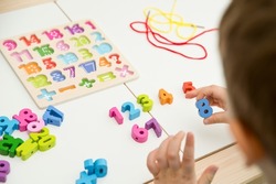 kid learning numbers through game. Sensory activity with wooden numbers and shoe laces. Educations at home, pre-school education, Montessori methodology. sequence of numbers, arithmetic problems.