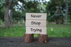 Motivational and creative concept; Wooden blocks arranged with words Never Stop Trying with nature background 